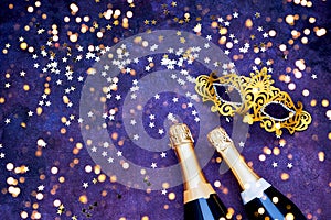 Two champagne bottles, golden carnival mask and confetti stars. Flat lay of Christmas, New Year, Purim, Carnival celebration