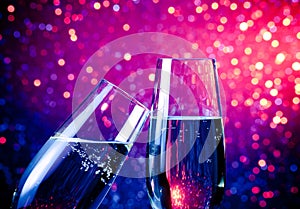 Two champagne flutes with gold bubbles on blue tint light bokeh background