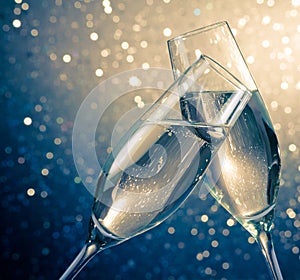 Two champagne flutes with golden bubbles on blue light bokeh background