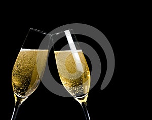 Two champagne flutes with golden bubbles make cheers on black background