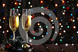 Two champagne glasses and Christmas decorations on the table on a dark background with a colored garland bokeh