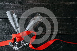 Two champagne glasses on a dark table tied with a red ribbon.