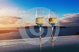 Two champagne glasses on the edge of infinity swimming pool at sunset on Santorini island