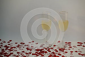 Two champagne glasses filled with wine surrounded by heart shaped confetti