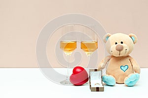 Two champagne glasses and gift box with golden ring teddy bear toy and red heart on white background with copy space. valentines