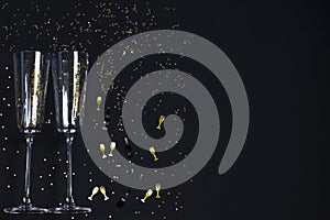 Two champagne glasses, golden confetti on a festive black background. Festive Christmas, New Year concept. Copy space
