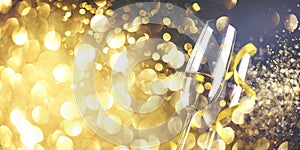 Two champagne glasses with golden ribbon and gold glitter splash bokeh on dark background. Luxury restaurant dinner celebration.