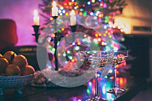 Two champagne glasses on illuminated christmas tree defocused background