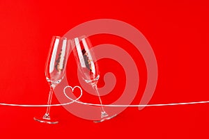 Two champagne glasses with red heart shaped confetti over red background