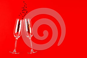 Two champagne glasses with red heart shaped confetti over red background