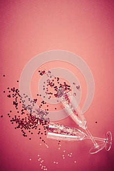 Two champagne glasses with splash of red heart shaped confetti on red background