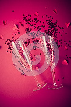 Two champagne glasses with splash of red heart shaped confetti on red background