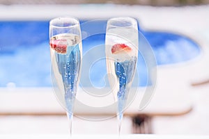 Two champagne glasses with strawberry on sunny terrace outdoor patio overlooking swimming pool at summer day outside of