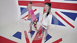 Two charismatic girls in t-shirts look at camera and synchronically dance