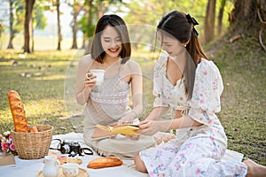 Two charming Asian women having an afternoon tea party in the park together, enjoy picnicking
