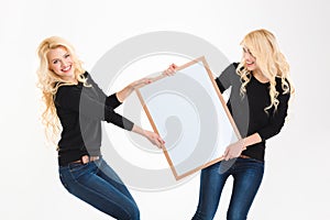 Two charming blonde sisters twins having fun holding blank board