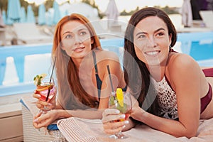 Two charming female friends relaxing by the swimming pool