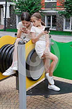 two charming teenage girls in identical clothes with smartphones outside. kids surf the net. smartphone addiction