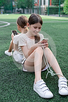 two charming teenage girls in identical clothes with smartphones outside. kids surf the net. smartphone addiction
