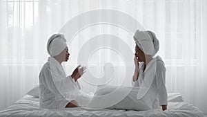 Two Cheerful African American Sisters Wearing Bathrobes Chatting And Laughing At Home