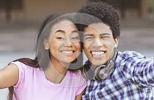 Two cheerful african teenagers taking selfie outdoors