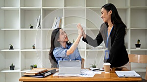 Two cheerful Asian businesswomen are giving high fives to each other while working together