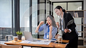 Two cheerful Asian businesswomen are looking at a laptop screen with a happy face