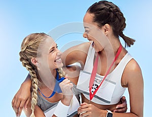 Two cheerful athletic women embracing while holding gold medals from competing in sports event. Joyful fit active