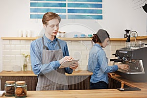 Two cheerful baristas in stylish uniform wroking at bar counter.