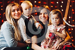 Two mothers sitting with cute kids christmas presents.