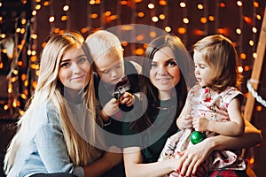 Two mothers sitting with cute kids christmas presents.