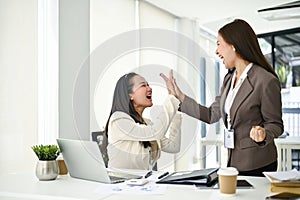 Two cheerful businesswomen are giving high fives to cheer each other up