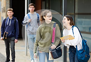 Two cheerful carefree female students walking down street