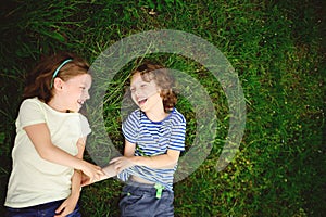 Two cheerful children lie on a green grass.