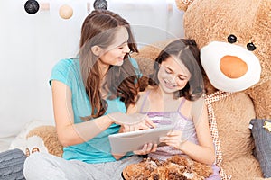 Two cheerful cute sisters sitting and using tablet together