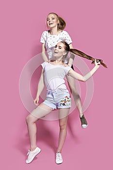 Two cheerful excited young women jumping and having fun together over pink background