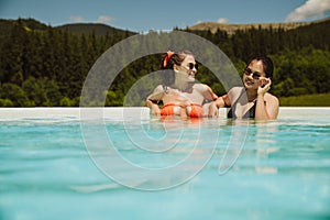 Two cheerful female friends relaxing in pool during vacation in mountains