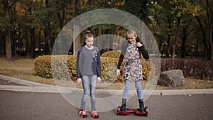 Two cheerful friends ride and dance on an electronic scooter in an autumn park.