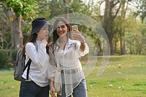Two cheerful friends taking selfie on smartphone while walking in campus at sunset with a warm light.