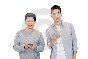 Two cheerful friends wear gray t-shirts standing isolated over white background, holding mobile phone.Couple of cool guys using