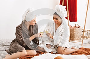 Two cheerful girlfriends having spa day together, drinking champagne