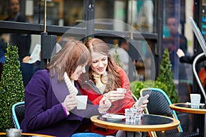 Two cheerful girls drinking coffee in a Parisian street cafe