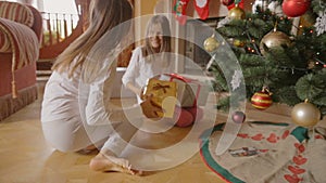 Two cheerful girls running to the gifts under Christmas tree at morning