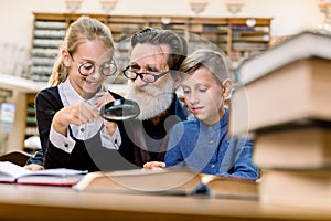 Two cheerful happy kids, boy and girl with magnifying glass glass listening to interesting book story from their