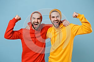 Two cheerful hipster men guys in fashion red yellow clothes posing isolated on pastel blue background studio portrait