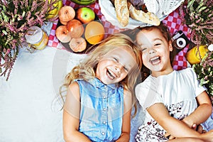 Two cheerful kids lying on a picnic blanket among refreshments