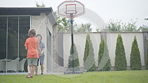Two cheerful little boys playing basketball at home. Portrait of happy relaxed Caucasian schoolboys resting on weekends