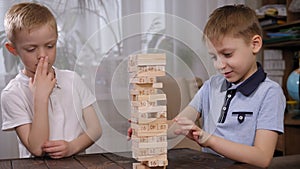 Two cheerful little boys are playing a board game with wooden blocks at home.