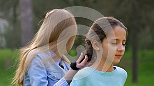 Two cheerful little girl to do hairstyles outdoors. braiding plait