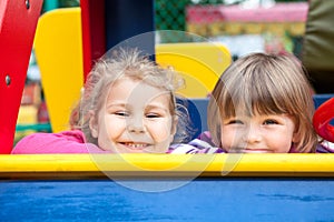 Two cheerful little girls laughing while sitting in frame of children playground, foxlike behaviour